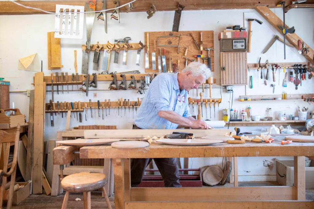 Charlie Shackleton hand planes a piece of wood in his workshop at ShackletonThomas in Bridgewater. Charlie and his wife, potter Miranda Thomas, established ShackletonThomas in 1987. Photo by Erica Houskeeper.